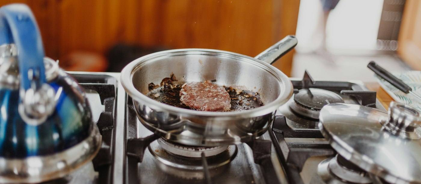 Een RVS koekenpan met vlees op een gasfornuis